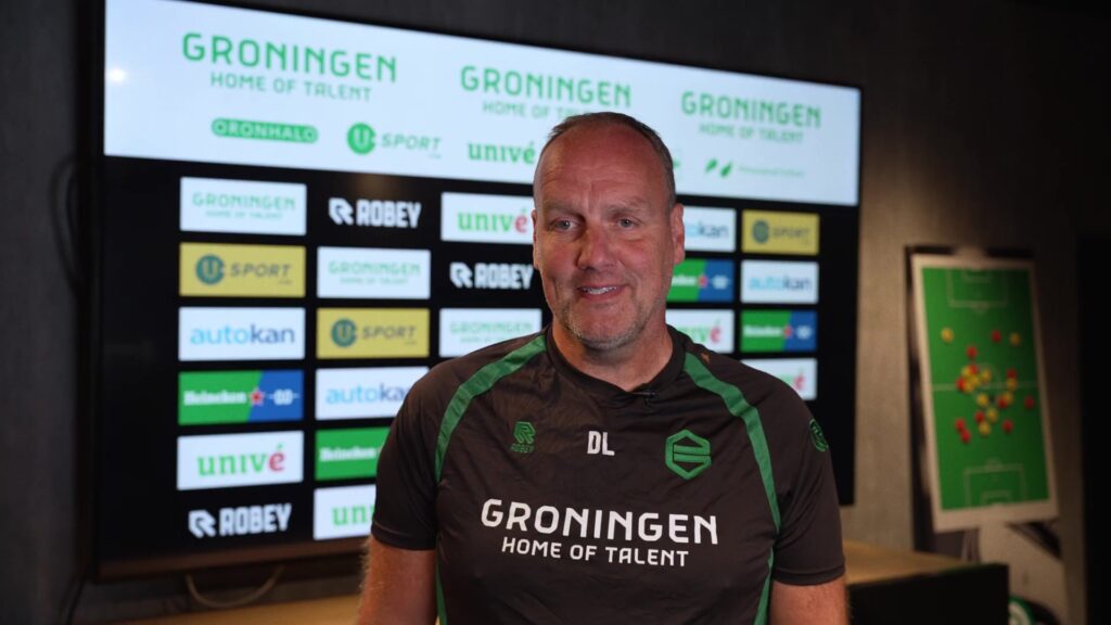 Trainer Dick Lukkien van FC Groningen voor het sponsorbord in het clubhuis